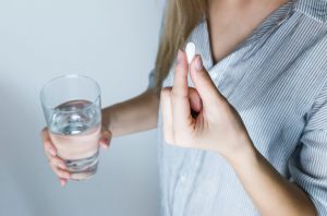 Woman Holding Half-full Glass and White Medicine Pill