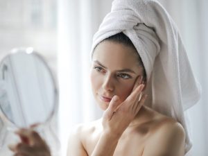 Woman with hair in towel looking at skin in mirror