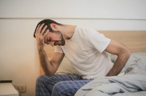 Young man holding head sitting in bed with pain