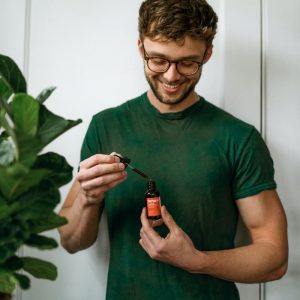 Man in green shirt holding Tanasi CBD Tincture with dropper 