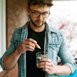 Man in jean jacket holding Tanasi Water Soluble and glass of water