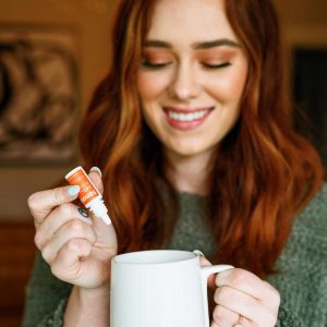 Woman with red hair smiling and using Tanasi CBD water soluble in coffee mug