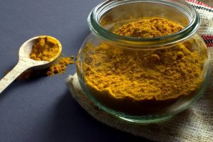 Turmeric spice in a clear jar with wooden spoon