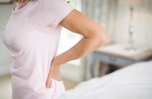 Woman in pink shirt holding her back from kidney pain
