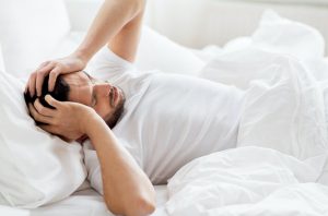 man suffering from hangover headache laying in bed